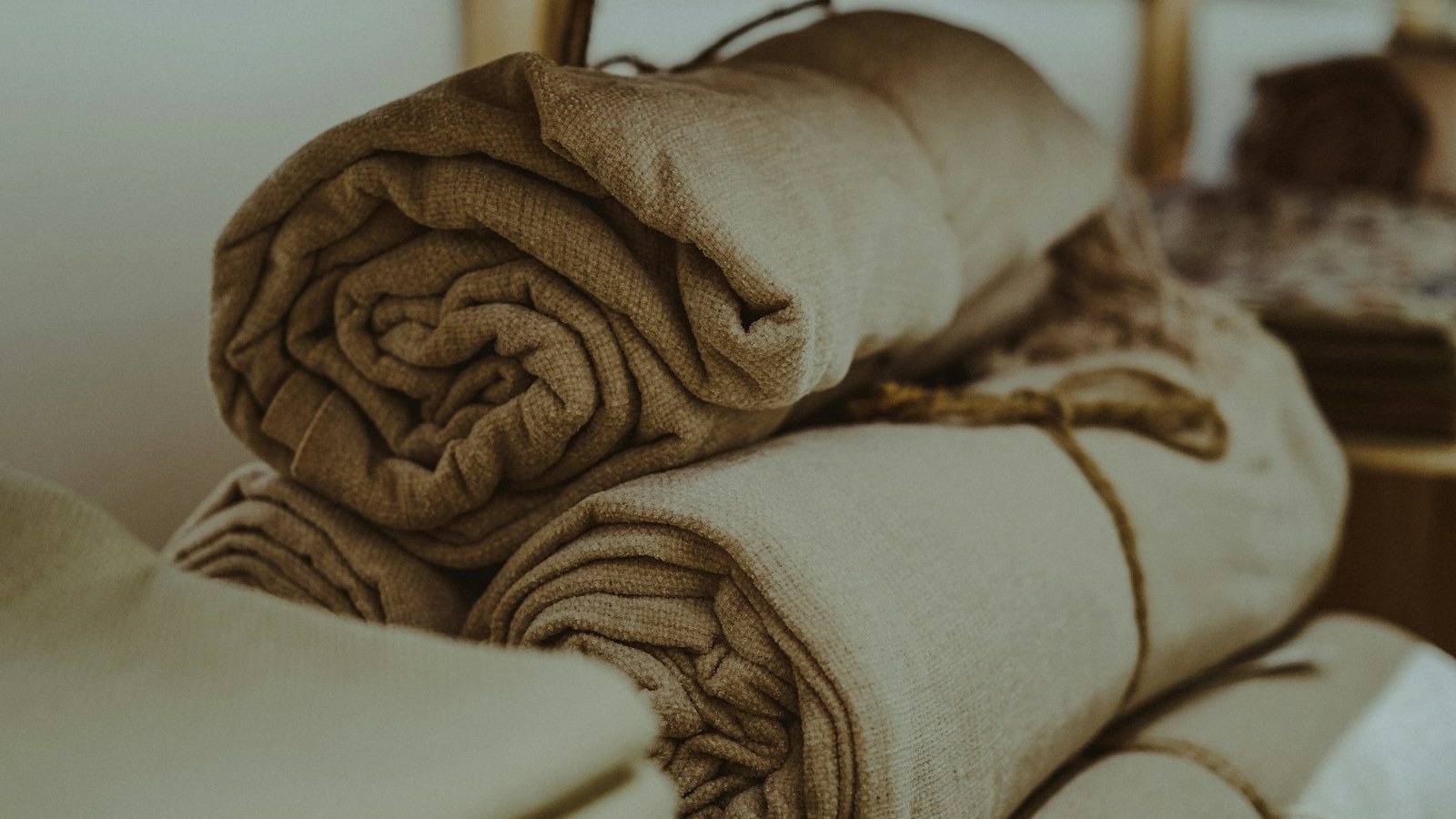Folded and rolled linen cloths in oatmeal and cream stacked on an oak shelf